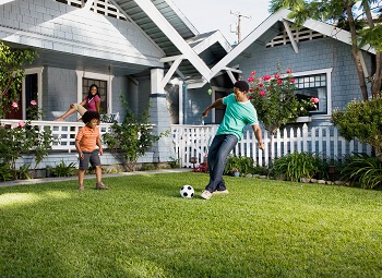 Family of three, father and son playing soccer in the backyard while mom sits on the porch and watches
