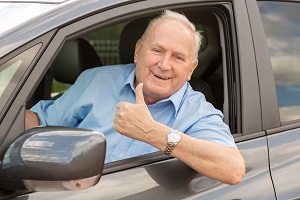 older man in the drivers seat smiling at the camera